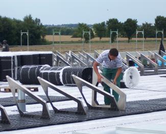 Fixodrain® XD 20 is just the right foundation for combining green and solar – and it provides for drainage across the entire area beneath the solar energy system. Man installs solar base frames on a green roof
